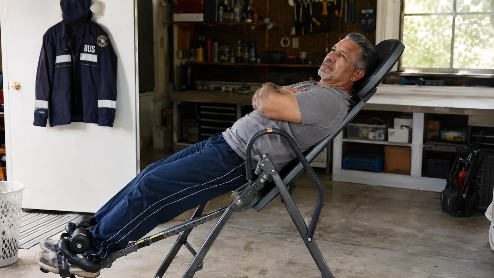 Middle-aged man using a YOLEO inversion table in a home garage, partially tilted back with hands relaxed