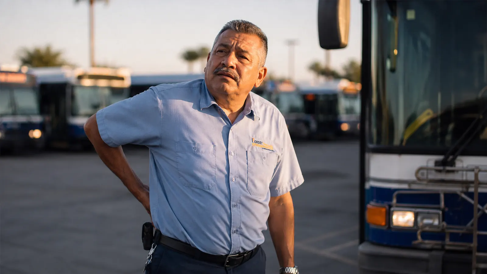 A tired city bus driver in uniform stretching his lower back beside his parked bus at the end of a shift