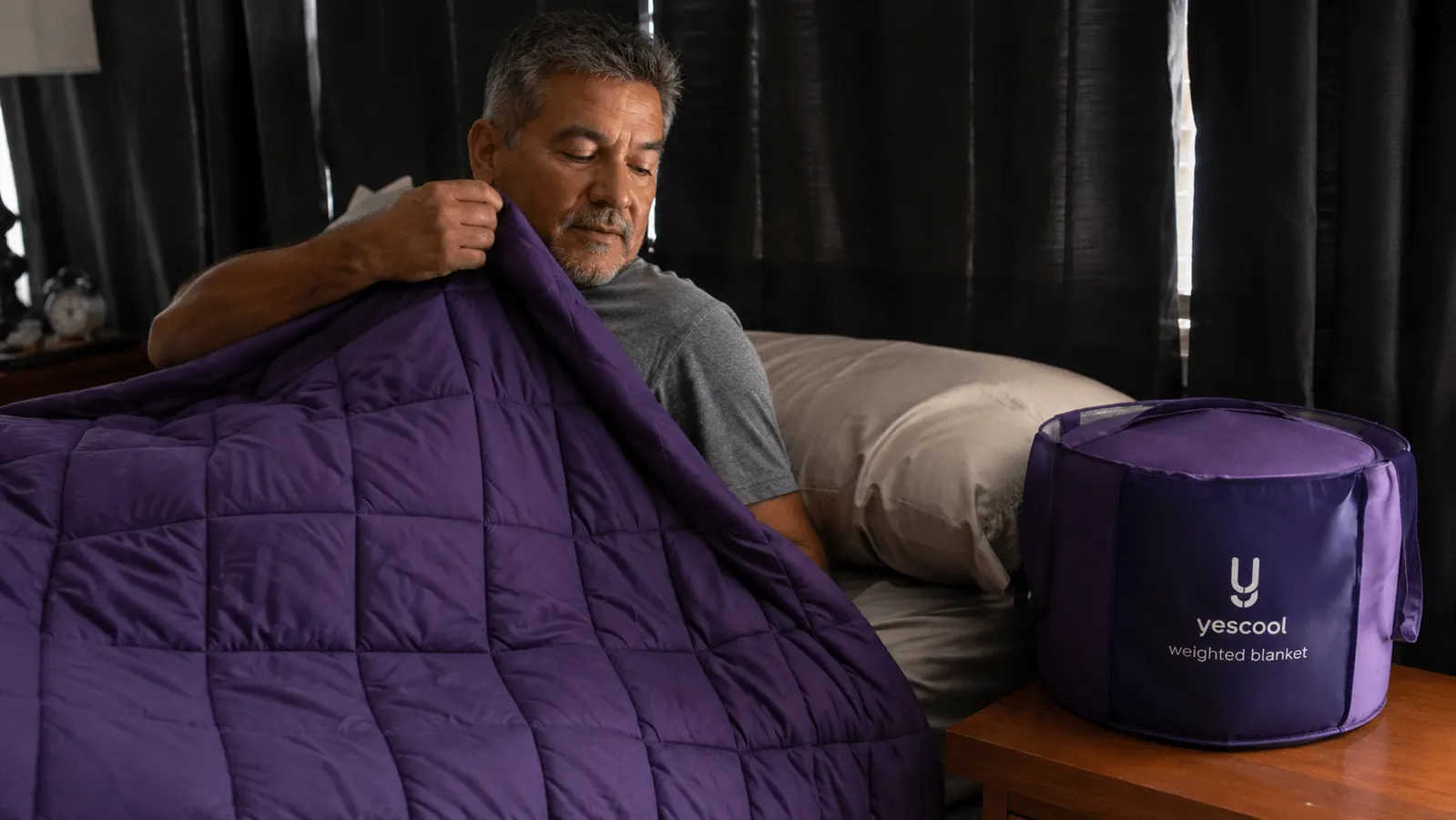 Man in a bus driver uniform shirt pulling a purple weighted blanket over himself while lying down for a daytime nap