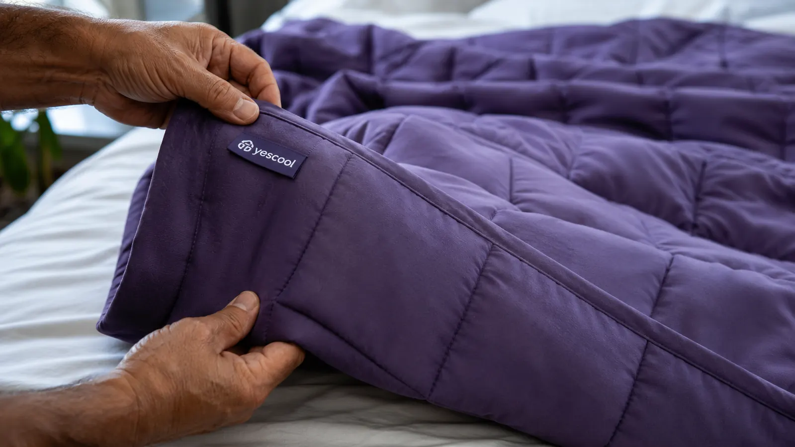 Hands pulling back the foot-end corner of a purple weighted blanket to show the fill compared to the center of the blanket