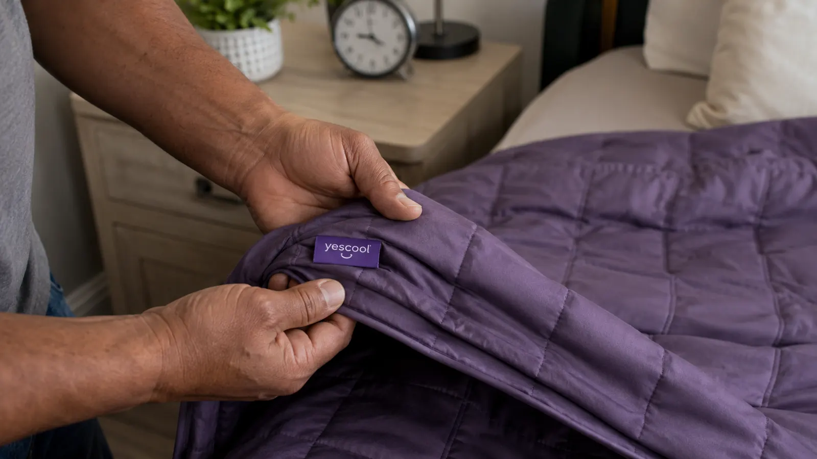 Close-up of hands folding back the corner of a purple weighted blanket showing the glass bead fill and quilted grid stitching